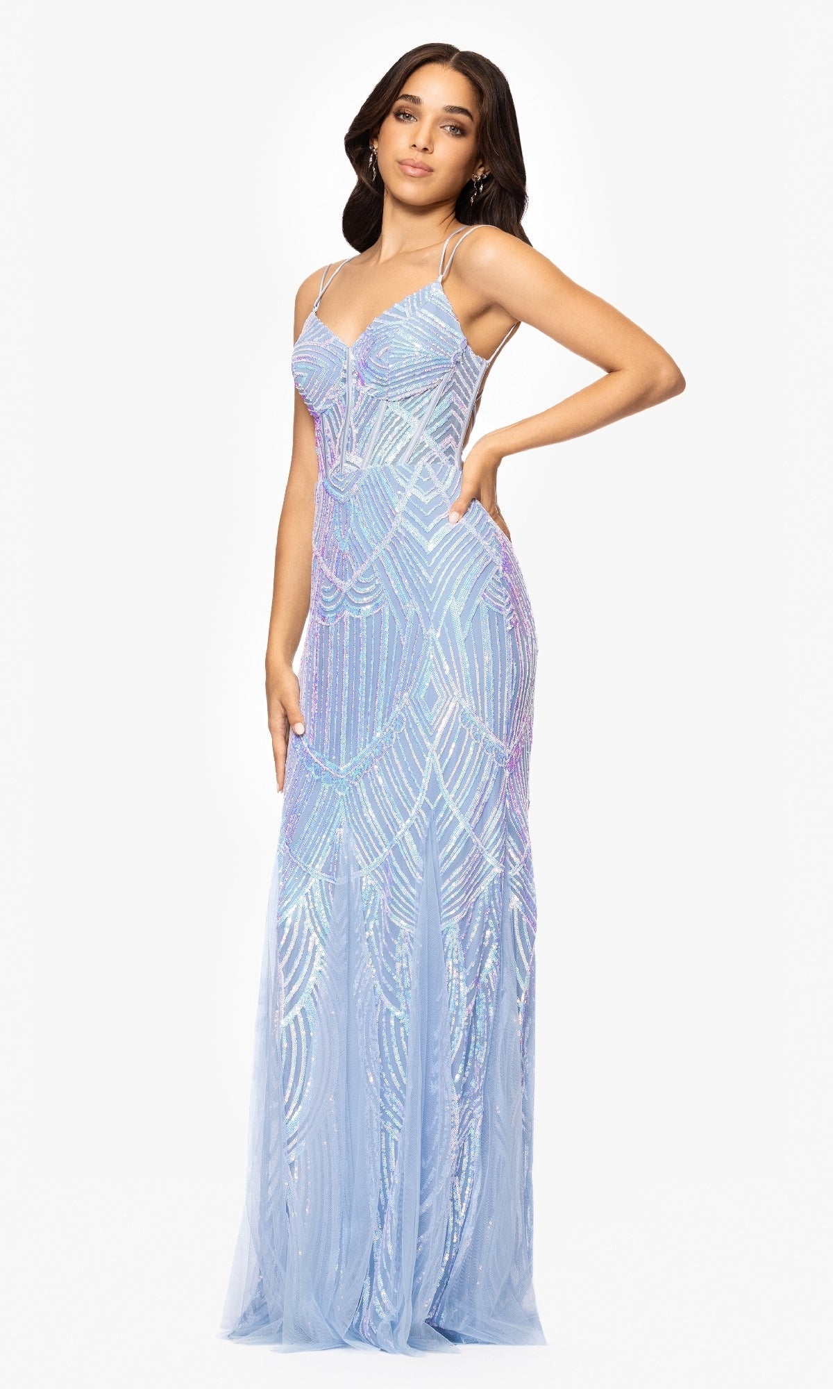 A woman poses with one hand on her hip in the Long Blue Sequin Prom Dress: Blondie Nites 5314BN, a floor-length gown featuring geometric sequin patterns, set against a white background.